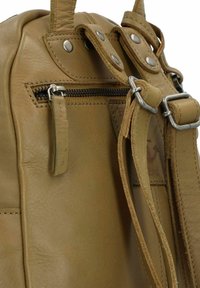 Mochila de cuero marrón con acentos metálicos. Cuenta con un cierre superior de cremallera, correas ajustables y un bolsillo lateral con cremallera. Textura suave.