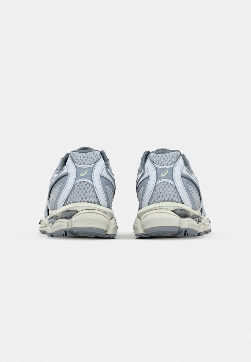 Graue Sportschuhe mit einem atmungsaktiven Obermaterial aus Mesh, gepolstertem Kragen und kontrastierenden weißen Akzenten, die eine gebogene Sohle und strukturierte Details zeigen.