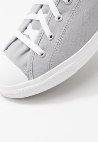 Szare płótniowe tenisówki z białą gumową czubką i podeszwą, z białymi sznurowadłami i metalowymi przelotkami, z teksturowanym wykończeniem z tkaniny na górze.