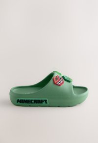 Claquette en plastique verte avec une semelle intérieure texturée, un talon surélevé et un logo "MINECRAFT" bien visible sur le côté, agrémenté d'accents colorés.