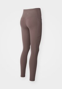 Leggings w wysokim stanem w kolorze mauve z kieszenią boczną, pokazane z tyłu, z gładkiego materiału i dopasowanym krojem.