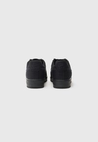 Sorte Nike Air-sneakers med overdel i semsket skinn og mesh, flate lisser, polstret krage og strukturert gummisåle, som viser et minimalistisk design.