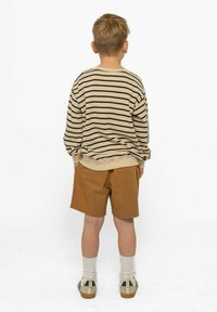 Camicia a maniche lunghe a righe beige e blu navy con polsini a coste, abbinata a pantaloni corti beige. Il modello indossa calze bianche e sandali beige.