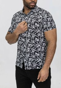 Chemise à manches courtes noire avec imprimé floral blanc, patte de boutonnage à l'avant, col, et coupe ajustée, portée avec un jean foncé.