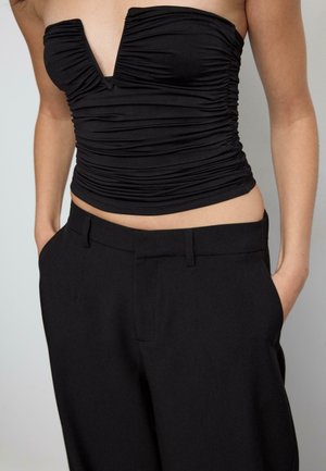 Musta rypytetty yläosa, jossa syvä V-pääntie, yhdistettynä korkeavyötäröisiin mustiin räätälöityihin housuihin. Molemmissa vaatekappaleissa on sileä pinta ja ne istuvat hyvin.