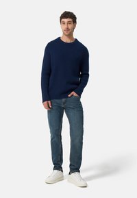 Dunkelblauer Rippstrick-Pullover, entspannte Passform, runder Halsausschnitt. Kombiniert mit hellblauen Jeans und weißen Sneakern. Minimalistisches Design.