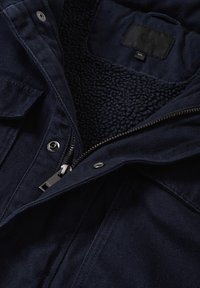 Veste bleu marine foncé avec fermeture éclair ouverte et doublure en polaire noire texturée visible à l'intérieur du col.