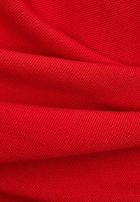 Tissu tissé rouge vif avec une texture visible et des plis doux créant des lignes courbes et des ombres.