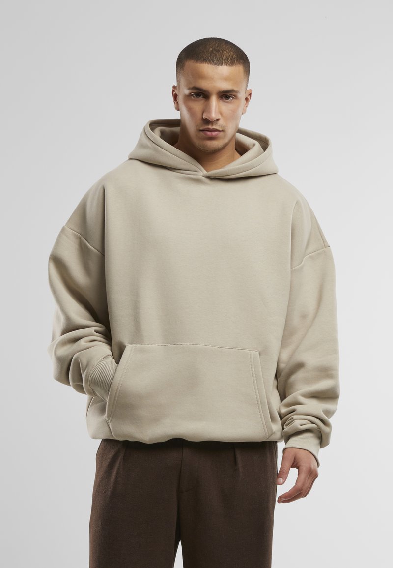 Hoodie oversize beige avec une poche avant et une capuche à cordon, fabriqué en tissu en coton doux ; doté d'épaules tombantes et de poignets côtelés.