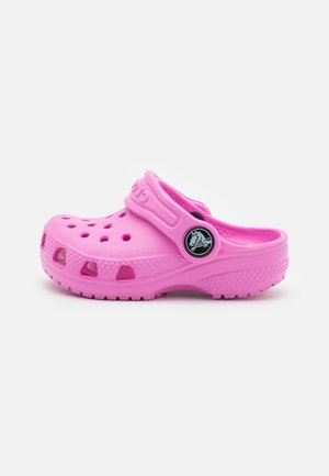Zuecos Crocs rosas con agujeros de ventilación, superficie texturizada y una correa para un ajuste seguro. Presentan un logo circular en el lateral.