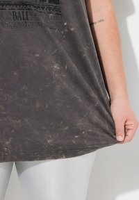 Sort, distressed bomulds t-shirt med Bali grafisk tryk i hvid, med en afslappet pasform. Sammen med skinnende sølv leggings.