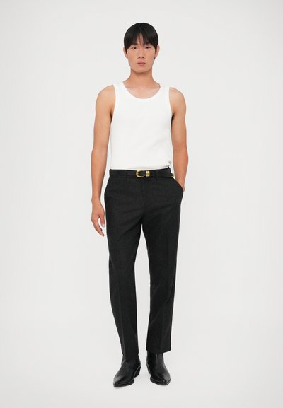 Top branco sem mangas e calças de fato cinza-escuro com um cinto preto com fivela dourada. As calças têm um corte reto e textura suave.