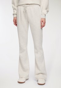 Jasnoszare dresowe spodnie o szerokim kroju, z wąskim paskiem w talii i miękką teksturą, w połączeniu z białymi trampkami o chropowatej powierzchni.