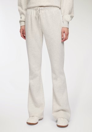 Pantaloni sportivi grigi chiari con design a gamba larga, vita con cordoncino e texture morbida, abbinati a sneaker bianche con superficie texturizzata.