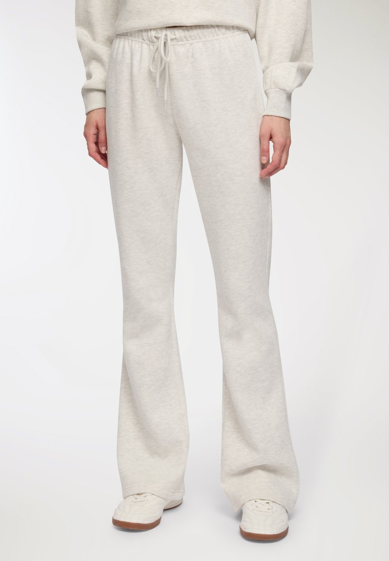 Jasnoszare dresowe spodnie o szerokim kroju, z wąskim paskiem w talii i miękką teksturą, w połączeniu z białymi trampkami o chropowatej powierzchni.