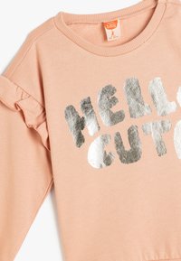 Lyserød sweatshirt med flæseærmedetalje og sølvfolieprint med teksten "HELLO CUTE." Blødt, textured stof, crew neck design.