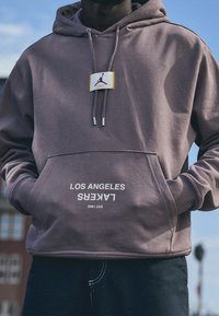 Felpa viola con tasca frontale, caratterizzata da una stampa bianca "LOS ANGELES LAKERS" e un patch con il logo Jordan vicino al colletto.