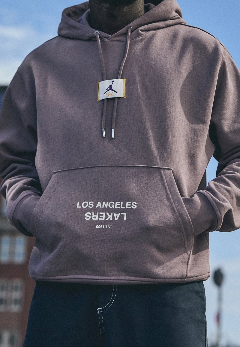 Felpa viola con tasca frontale, caratterizzata da una stampa bianca "LOS ANGELES LAKERS" e un patch con il logo Jordan vicino al colletto.