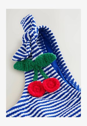 Tissu rayé bleu et blanc avec un accent noué. Présente une feuille au crochet verte et deux cerises au crochet rouges comme détails décoratifs.