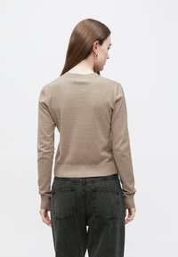 Béžový pletený svetr s dlouhými rukávy, zaobleným výstřihem, žebrovanými manžetami a lemem, nošený přes tmavě šedé džíny. Hladká textura, volný střih.
