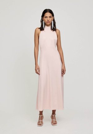 Langes, rosafarbenes ärmelloses Kleid mit hohem Kragen, glatter Textur und A-Linien-Silhouette. Kombiniert mit weißen Sandalen mit Riemchen.