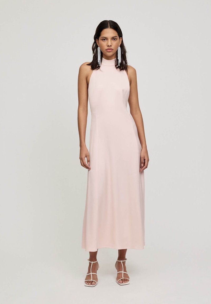 Lichtroze, mouwloze maxidress met een hoge hals. Gladde stof met een aansluitende lijfje en een losse, vloeiende rok. Geaccentueerd met sleehakken.