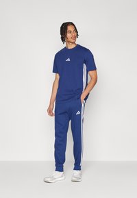 Survêtement de sport bleu marine avec un t-shirt arborant un petit logo blanc et un pantalon assorti avec des bandes blanches sur les côtés et des poignets côtelés.