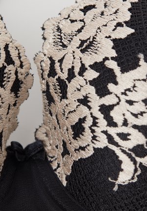 Tela negra texturizada con bordado floral beige en una sección ajustada de la prenda.