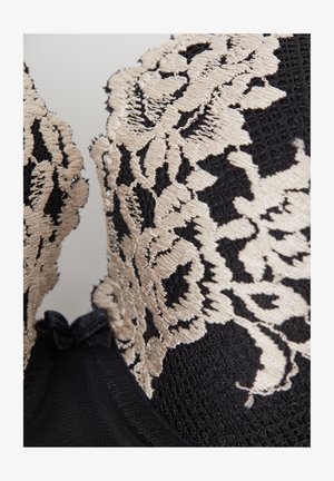 Tela negra texturizada con bordado floral beige en una sección ajustada de la prenda.