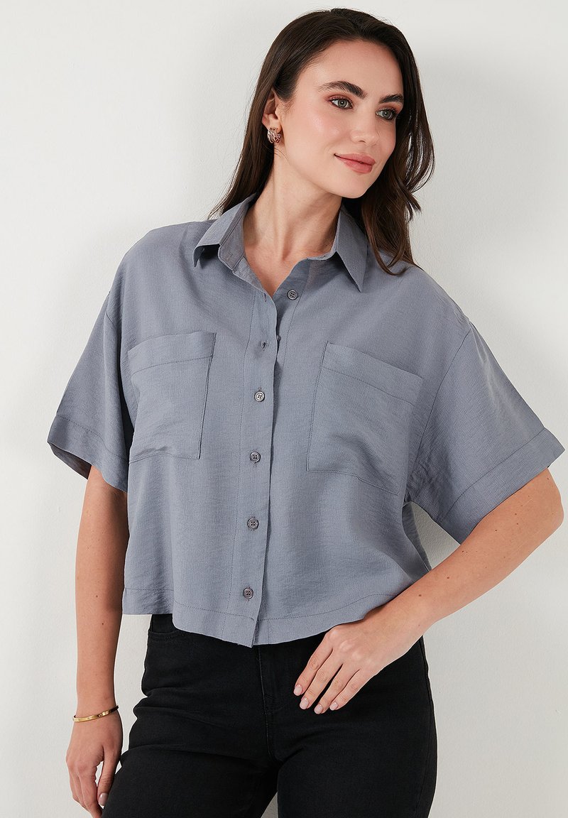 Camicia a maniche corte, con bottoni, in morbido tessuto grigio, caratterizzata da due tasche frontali e colletto. Tessuto liscio, vestibilità rilassata.