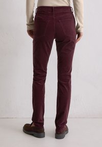 Bordowe spodnie ze sztruksu o dopasowanym kroju, z pięcioma kieszeniami, widocznymi przeszyciami i średnim stanem, zestawione z brązowymi butami.