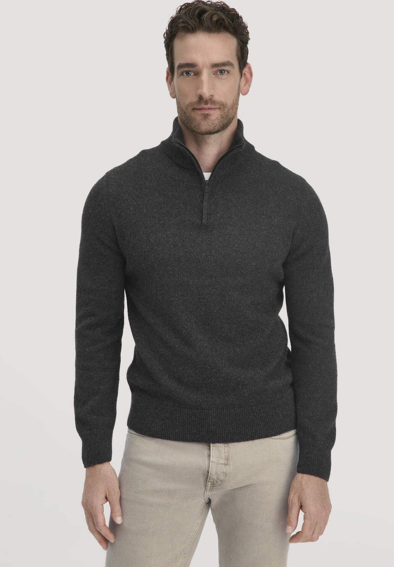 Dunkelgrauer Zip-Pullover aus weichem, strukturiertem Stoff. Figurbetontes Design mit langen Ärmeln und gerippten Bündchen und Saum. Kombiniert mit hellen Hosen.