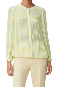 Blusa giallo chiaro con design a pieghe, scollatura rotonda e tessuto traslucido con sottili motivi blu, completata da chiusure a bottone.