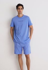Svetlo modré bavlnené tričko s krátkymi rukávmi a okrúhlym výstrihom, s nenápadným logom Calvin Klein, doplnené o zodpovedajúce šortky.