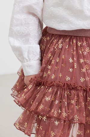 Bordeaux tulle nederdel med volanger, prydet med guld sløjfemønstre. Sammen med en hvid bluse med broderet sløjfedesign.