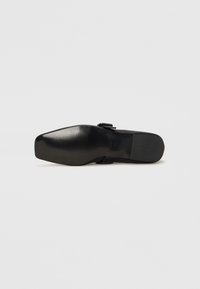 Semelle de chaussure noire avec un bout arrondi, surface plate et un motif de grip texturé. Présente une petite boucle et un design de talon bas.