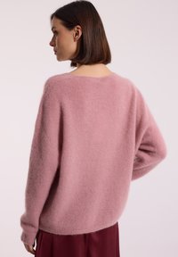 Różowy puszysty sweter z okrągłym dekoltem, opadającymi ramionami i długimi rękawami; charakteryzuje się miękką teksturą i luźnym krojem.