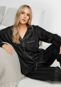 Svart satin pyjamas-set med randig mönster, som inkluderar en knappad skjorta, fickdetalj och pipade accenter. Mjuk textur och avslappnad passform.