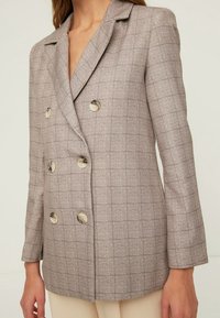 Blazer doppiopetto in tessuto a quadri marrone chiaro. Presenta rever a lancia, due file di bottoni metallici e maniche lunghe con vestibilità su misura.