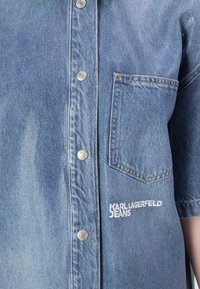 Τζιν πουκάμισο σε ανοιχτό μπλε χρώμα με ασημένια κουμπιά κλίκ, κοντά μανίκια, τσέπη στο στήθος και λευκή κεντημένη επιγραφή "Karl Lagerfeld Jeans".