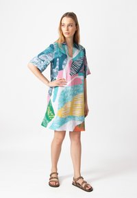 Lyhythihainen mekko, jossa on eläväinen, abstrakti kuvio teal-värissä, pinkissä, oranssissa ja keltaisessa. Valmistettu kevyestä ja hengittävästä materiaalista.