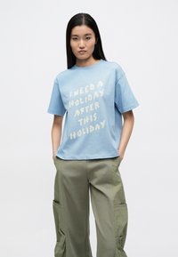 Ανοιχτό μπλε βαμβακερό μπλουζάκι με κοντά μανίκια που φέρει λευκό κείμενο με την επιγραφή "ΧΡΕΙΑΖΟΜΑΙ ΔΙΑΚΟΠΕΣ ΜΕΤΑ ΑΠΟ ΑΥΤΕΣ ΤΙΣ ΔΙΑΚΟΠΕΣ."