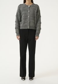 Cardigan grigio a trama con scollatura rotonda, cinque bottoni argentati e polsini a coste, abbinato a pantaloni neri e tacchi a punta.