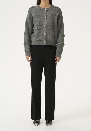 Grijze textuur cardigan met een ronde halslijn, vijf zilverkleurige knopen en geribde manchetten, gecombineerd met zwarte broeken en puntige hakken.