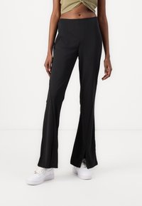 Czarne spodnie dzwony z bocznymi rozcięciami, wykonane z gładkiego, elastycznego materiału. Połączone z białymi trampkami dla uzyskania swobodnego wyglądu.