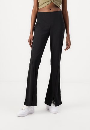 Sorte flare bukser med sideslids, lavet af et glat strækstof. Sammen med hvide sneakers for et afslappet look.