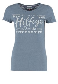 Camiseta de algodón azul con mangas cortas, que presenta el texto blanco "NEW YORK CITY Hilfiger Denim" y diseños triangulares. Corte casual y cuello redondo.