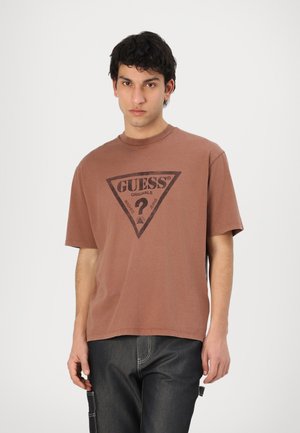 Brown cotton t-shirt with a triangular black logo featuring the word "GUESS" and a question mark, short sleeves, and a crew neckline.