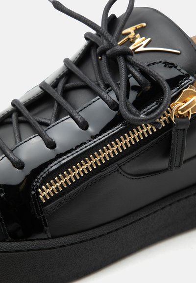 Μαύρο αθλητικό παπούτσι από γυαλιστερό δέρμα με μαύρα κορδόνια, χρυσή λεπτομέρεια φερμουάρ και χρυσό λογότυπο υπογραφής στη γλώσσα.