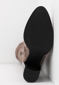 Botín de ante marrón hasta el tobillo con puntera redondeada, que presenta una suela de goma negra texturizada y un pequeño tacón. Tamaño 37 indicado en la plantilla interior.